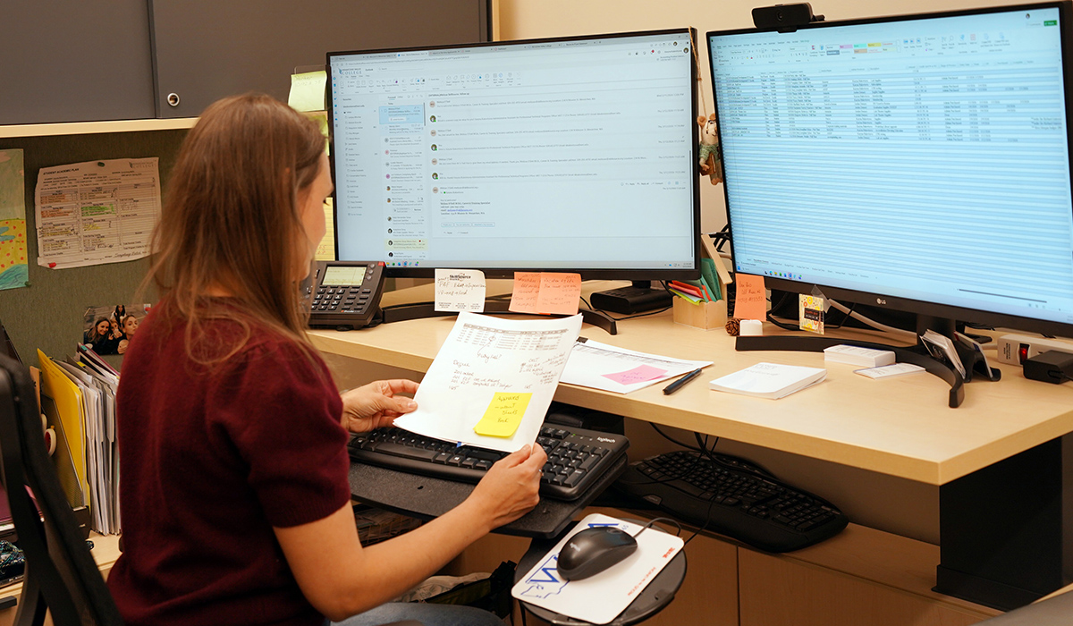 Office assistant working at a desk with two monitors