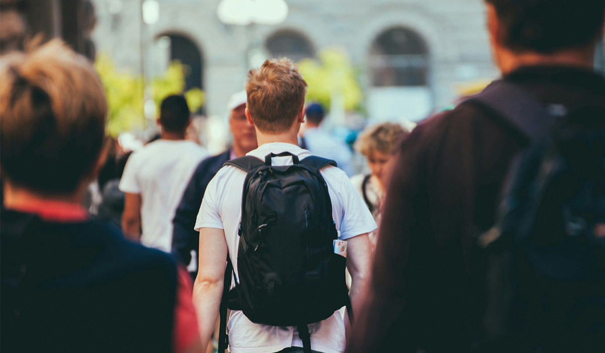 A student wearing a backpack walks through a crowd of people.