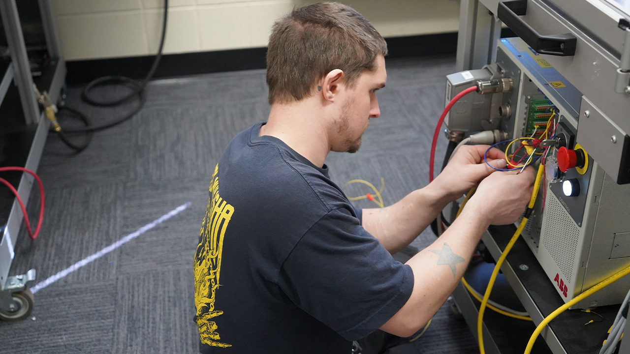 A student works on the wires that control a robotic arm.
