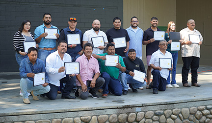 Two rows of WVC HOEEP graduates stand on a concrete stage and hold their graduation certificates.